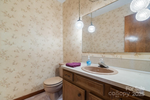 bathroom with toilet, wallpapered walls, and vanity