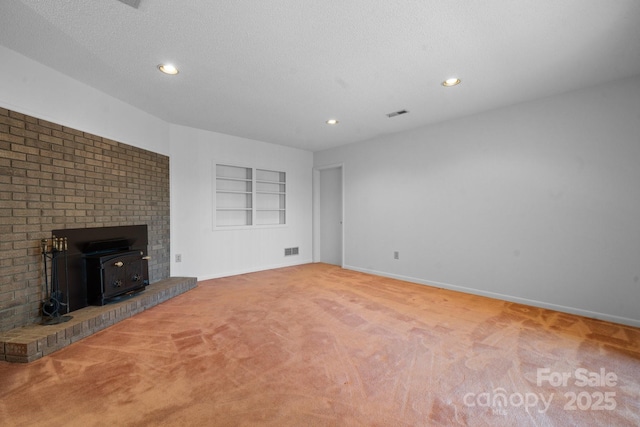 unfurnished living room with baseboards, visible vents, built in features, a wood stove, and a textured ceiling