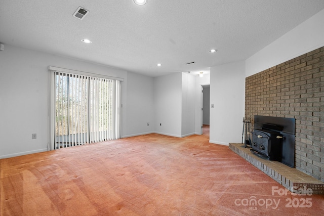 unfurnished living room featuring a wood stove, visible vents, light carpet, and a textured ceiling