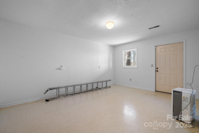 spare room with light floors, baseboards, visible vents, and a textured ceiling