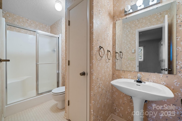 bathroom featuring a stall shower, a textured ceiling, toilet, and wallpapered walls