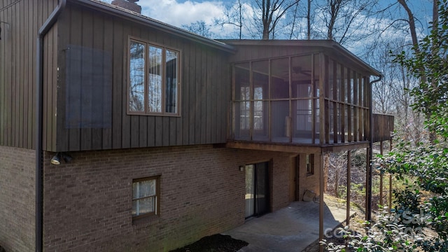 view of property exterior with a patio, brick siding, a chimney, and a sunroom