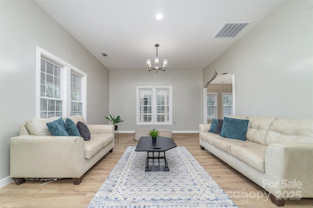 living area featuring a notable chandelier, light wood-style flooring, visible vents, and baseboards