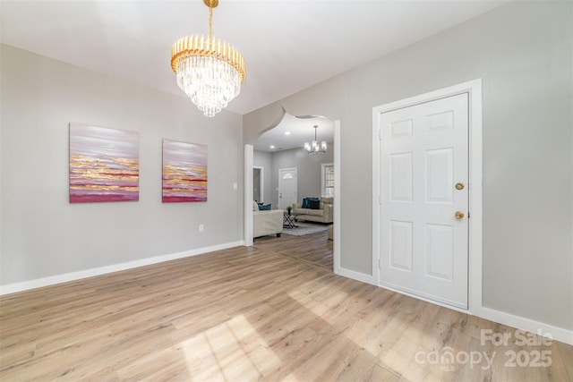 spare room with an inviting chandelier, baseboards, arched walkways, and wood finished floors