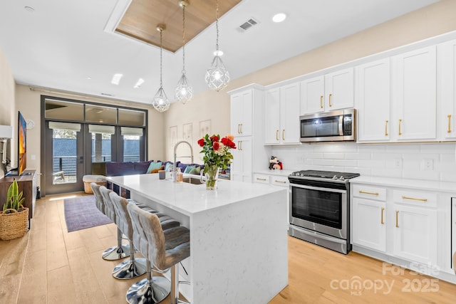 kitchen featuring an island with sink, appliances with stainless steel finishes, white cabinetry, and hanging light fixtures