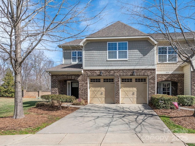 view of front of property featuring a garage, a shingled roof, concrete driveway, and brick siding