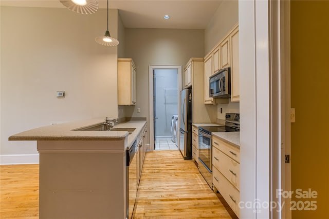 kitchen with light wood finished floors, a peninsula, stainless steel appliances, and a sink