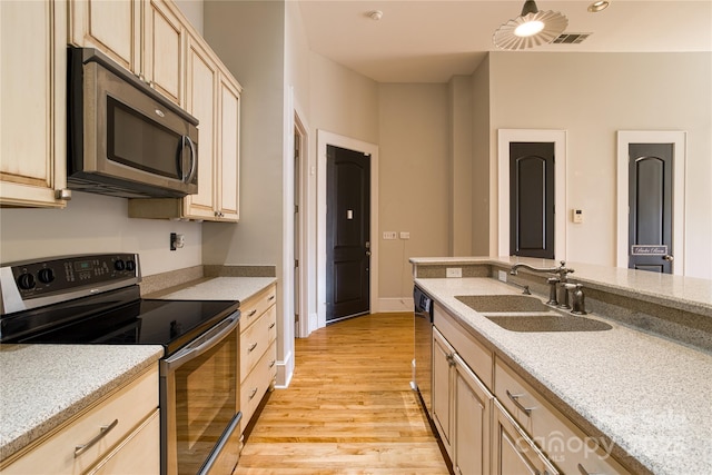 kitchen featuring light stone counters, a sink, light brown cabinetry, stainless steel appliances, and light wood-style floors