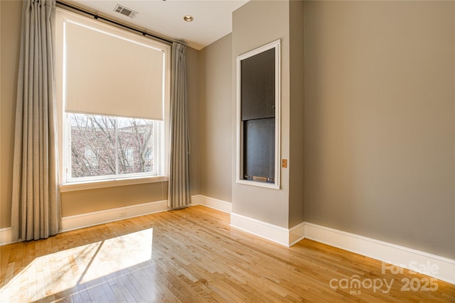 spare room with hardwood / wood-style flooring, baseboards, and visible vents