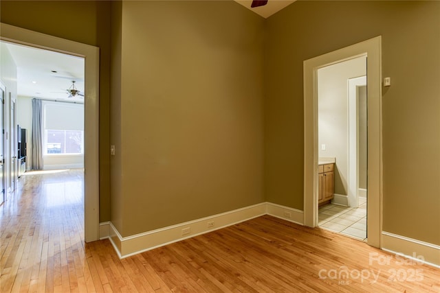 spare room with baseboards, light wood-style floors, and a ceiling fan