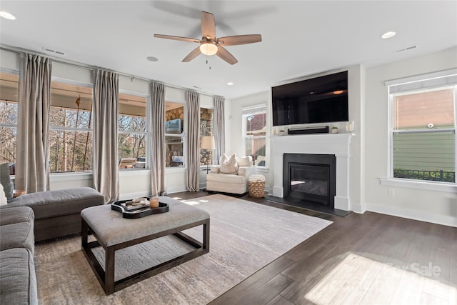 living room featuring a fireplace with flush hearth, recessed lighting, visible vents, and dark wood finished floors