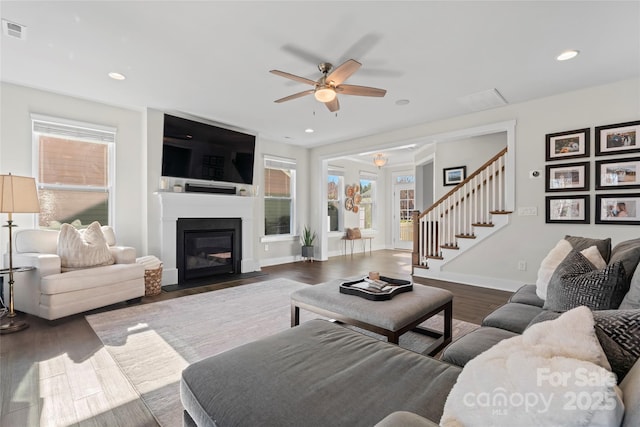 living area featuring recessed lighting, a fireplace with flush hearth, wood finished floors, visible vents, and stairs