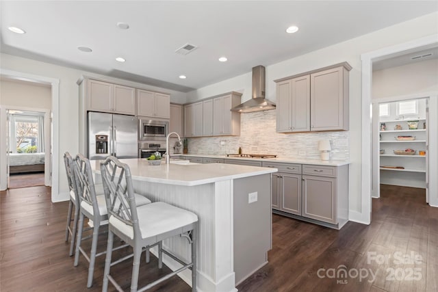 kitchen featuring visible vents, an island with sink, appliances with stainless steel finishes, light countertops, and wall chimney range hood