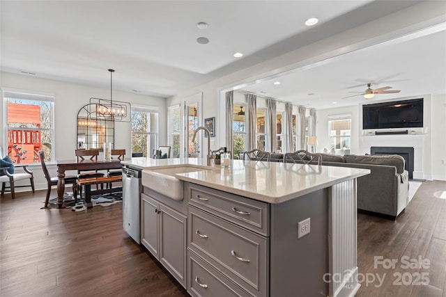 kitchen featuring pendant lighting, gray cabinets, open floor plan, a kitchen island with sink, and a sink