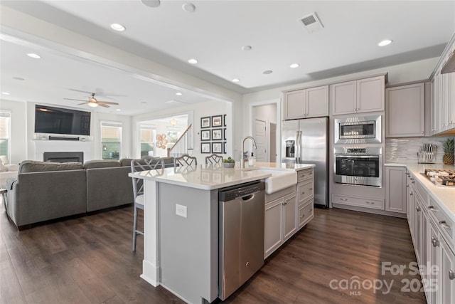 kitchen with open floor plan, stainless steel appliances, light countertops, and a kitchen island with sink