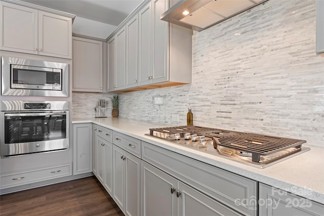 kitchen with tasteful backsplash, gray cabinets, light countertops, appliances with stainless steel finishes, and dark wood-type flooring