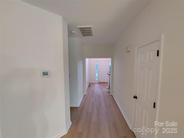 hallway with wood finished floors, visible vents, and baseboards