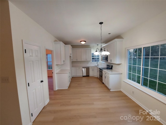 kitchen featuring white cabinets, stainless steel appliances, an inviting chandelier, and a sink