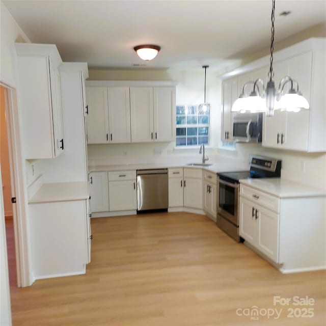 kitchen featuring a sink, stainless steel appliances, white cabinets, and hanging light fixtures