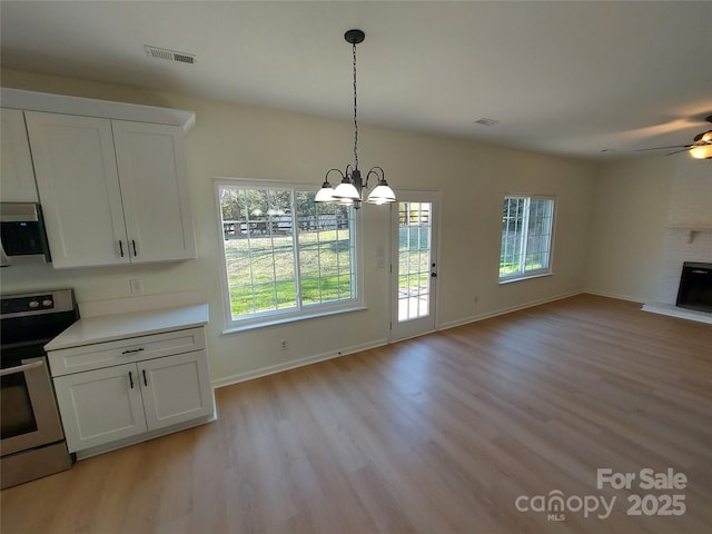 interior space featuring a brick fireplace, open floor plan, light wood-type flooring, electric range, and white cabinets