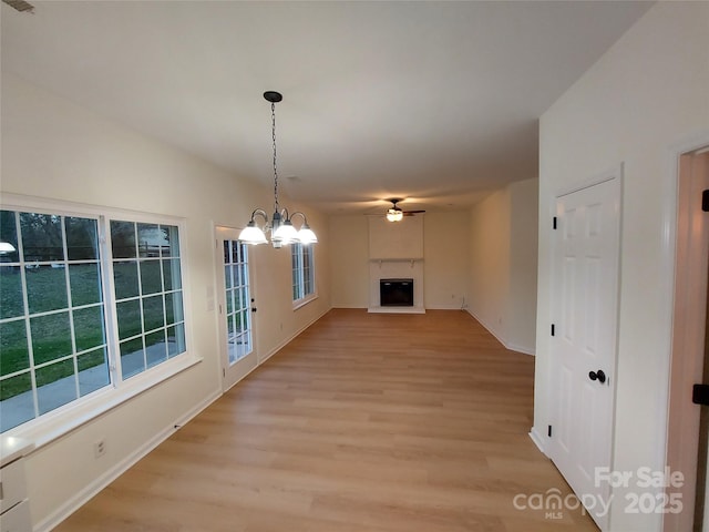 unfurnished dining area with baseboards, light wood-style flooring, a fireplace, and ceiling fan with notable chandelier