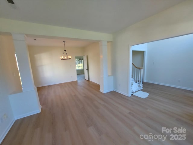 empty room featuring stairway, wood finished floors, baseboards, decorative columns, and a notable chandelier