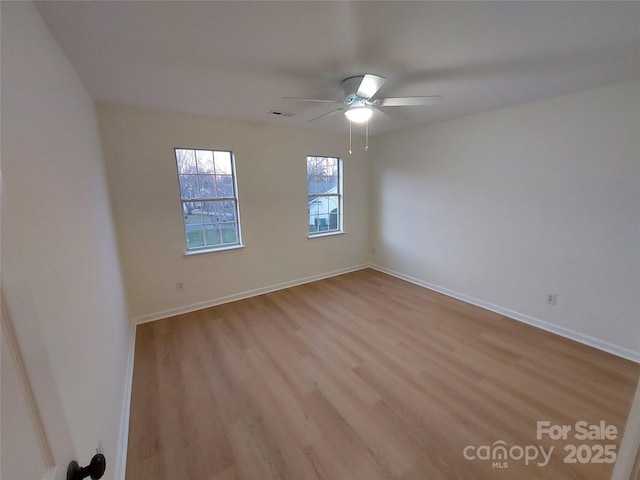 spare room with visible vents, ceiling fan, light wood-type flooring, and baseboards