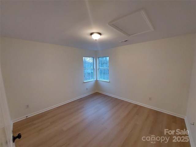 unfurnished room featuring attic access, wood finished floors, baseboards, and visible vents