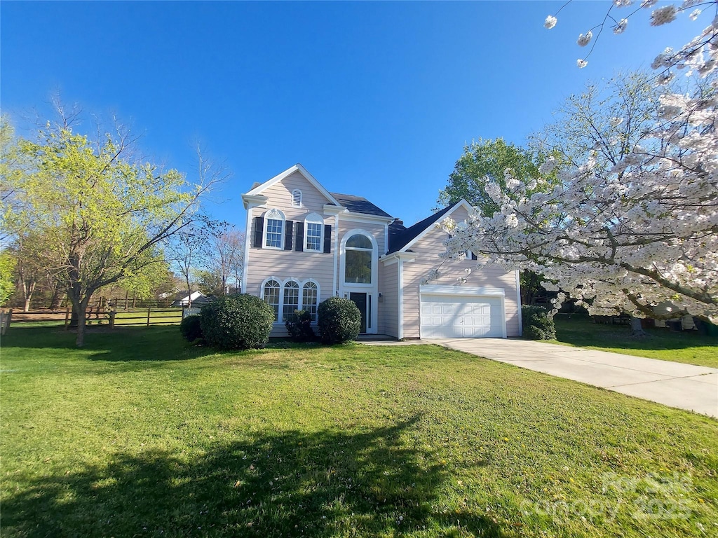 traditional-style home featuring a front yard, concrete driveway, fence, and an attached garage