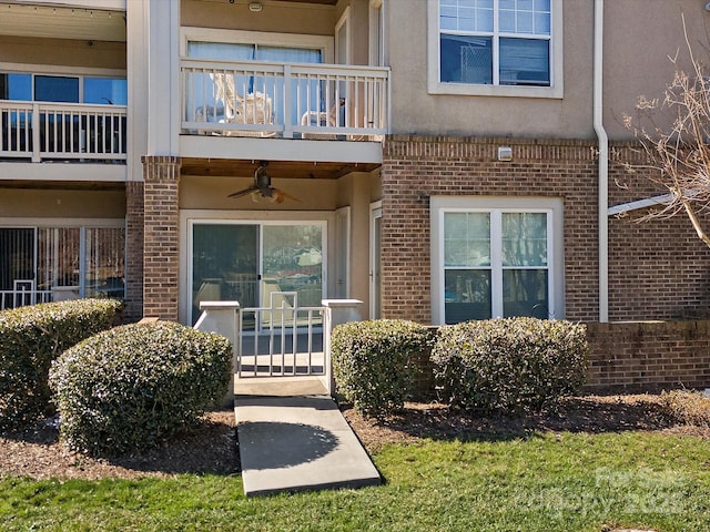 property entrance featuring a balcony, brick siding, a ceiling fan, and stucco siding