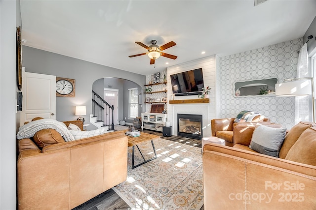 living room with arched walkways, a large fireplace, an accent wall, wood finished floors, and wallpapered walls