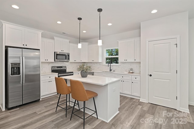 kitchen with a center island, stainless steel appliances, light countertops, hanging light fixtures, and white cabinets