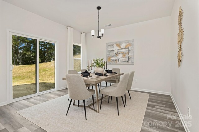 dining space with baseboards, visible vents, an inviting chandelier, and wood finished floors