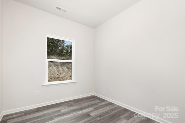 spare room with dark wood-style flooring, visible vents, and baseboards