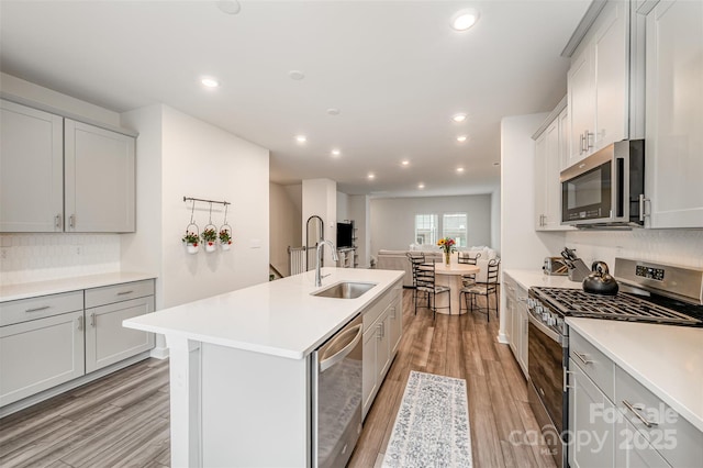 kitchen with a kitchen island with sink, light wood-style flooring, a sink, recessed lighting, and stainless steel appliances