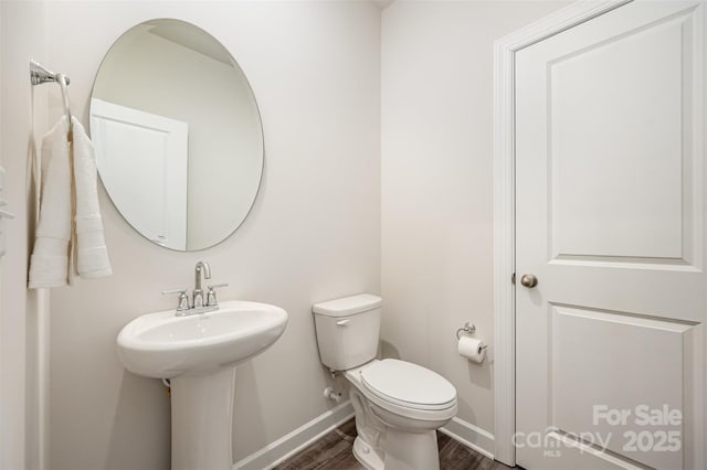 half bathroom featuring a sink, toilet, baseboards, and wood finished floors