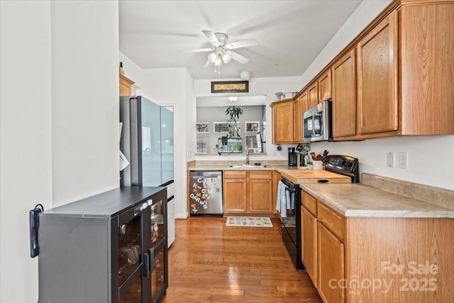 kitchen with light wood-type flooring, stainless steel appliances, ceiling fan, sink, and wine cooler