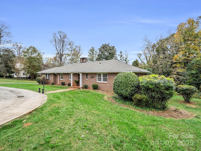 ranch-style home featuring concrete driveway, brick siding, a chimney, and a front yard