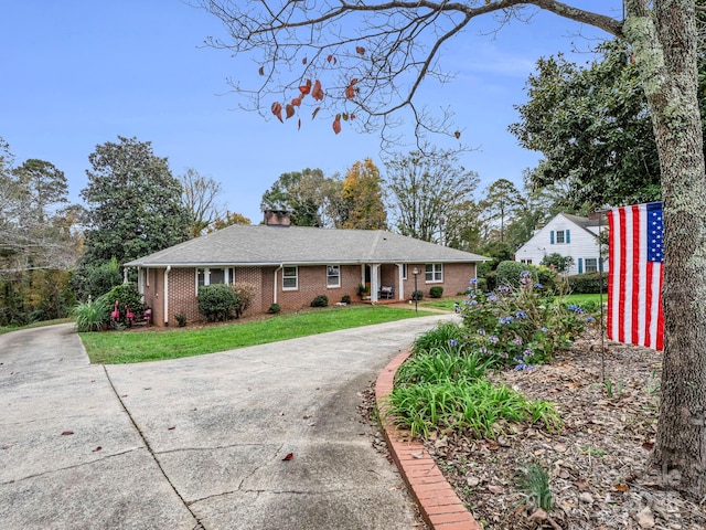 view of front facade with driveway, a front yard, a chimney, and brick siding