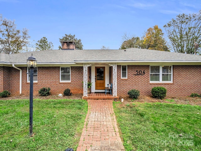 ranch-style home with roof with shingles, brick siding, a front lawn, and a chimney