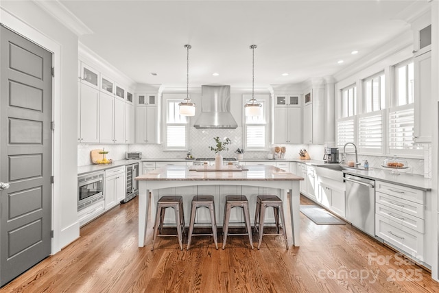 kitchen with beverage cooler, a sink, a kitchen island, appliances with stainless steel finishes, and wall chimney range hood