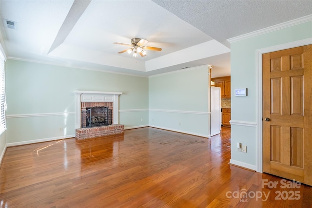 unfurnished living room featuring ceiling fan, light hardwood / wood-style floors, a raised ceiling, a brick fireplace, and crown molding