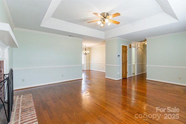 unfurnished living room featuring a fireplace, ornamental molding, a tray ceiling, hardwood / wood-style flooring, and ceiling fan with notable chandelier