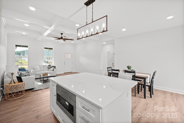 kitchen featuring stainless steel microwave, hanging light fixtures, open floor plan, white cabinets, and a kitchen island