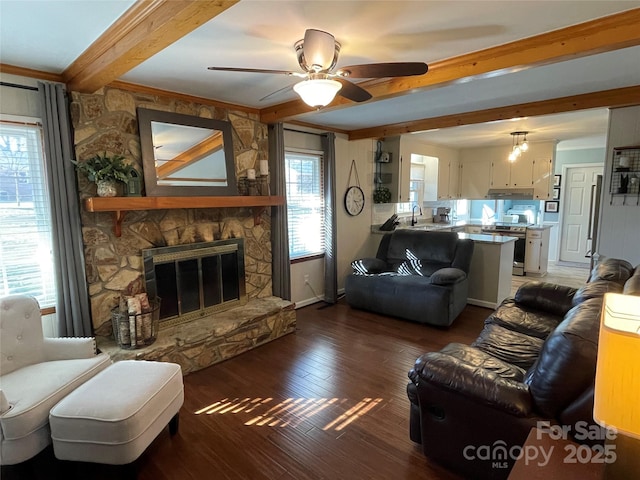 living room with sink, beamed ceiling, a stone fireplace, dark hardwood / wood-style floors, and ceiling fan