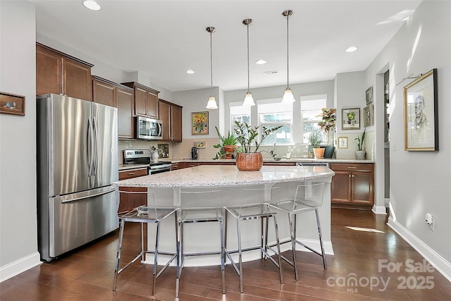 kitchen featuring appliances with stainless steel finishes, a center island, decorative light fixtures, dark wood-type flooring, and backsplash