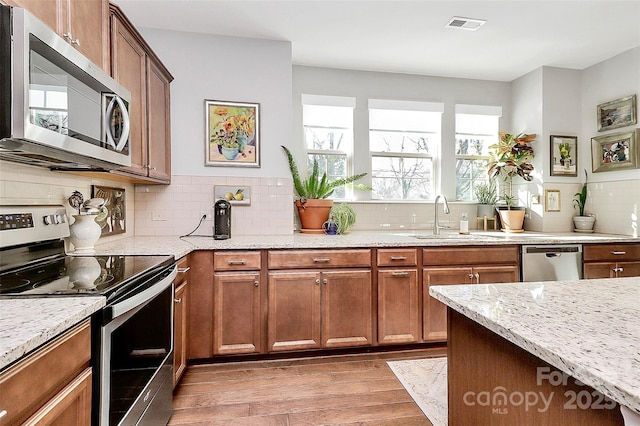 kitchen featuring a sink, visible vents, appliances with stainless steel finishes, light wood finished floors, and light stone countertops