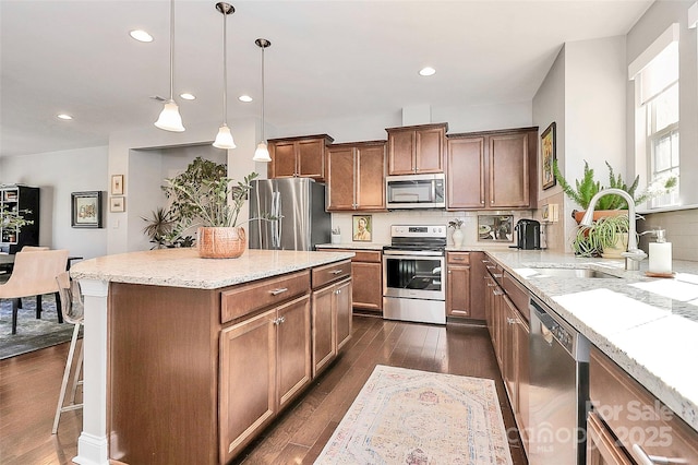 kitchen featuring a sink, a kitchen island, light stone counters, pendant lighting, and stainless steel appliances