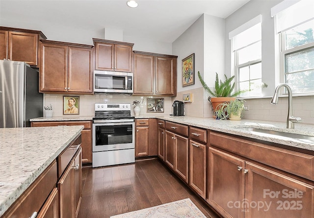 kitchen featuring a sink, light stone counters, dark wood-type flooring, stainless steel appliances, and tasteful backsplash