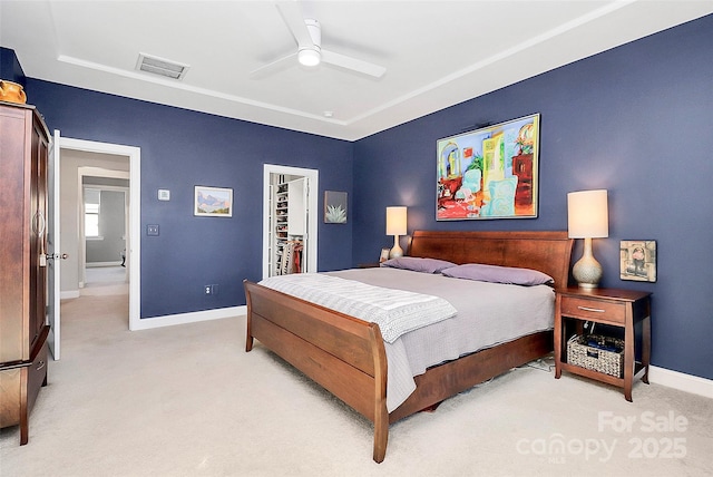 bedroom featuring baseboards, visible vents, a ceiling fan, light colored carpet, and a walk in closet